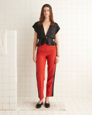 A person in a black top and scarlet Waterfront Trousers stands against a tiled white wall, exuding a 1940s-inspired charm.