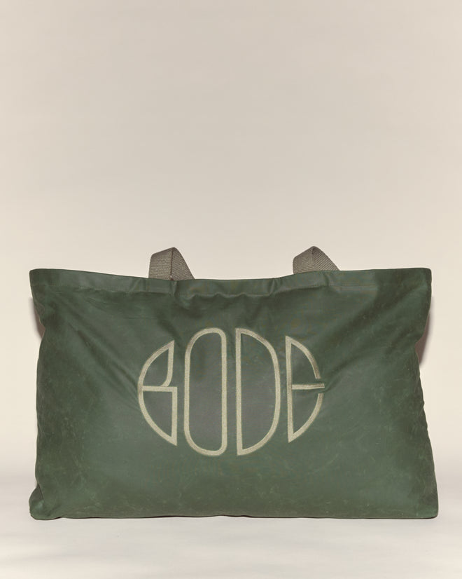 The Waxed Cotton Zip Tote - Green features gray handles and a bold, stylized embroidered Bode logo on the front. Crafted in Italy from green waxed cotton.
