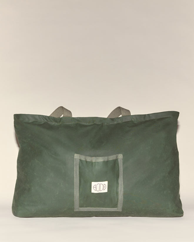 The Waxed Cotton Zip Tote - Green is a large green waxed cotton bag with gray handles, a front pocket, and an embroidered Bode logo. Made in Italy.