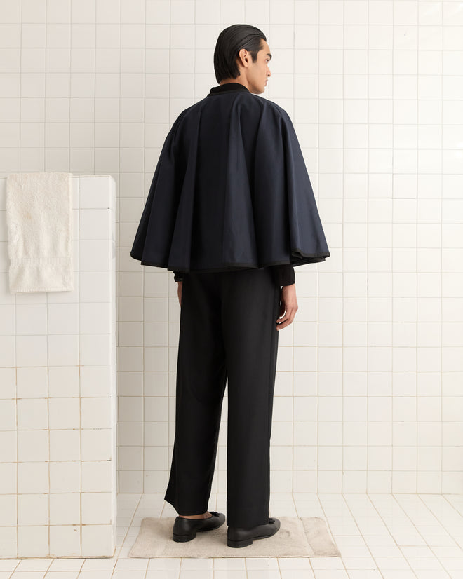 Dressed in a stylish Navy Waxed Herringbone Rain Cape, someone stands confidently on a bath mat in the tiled bathroom.