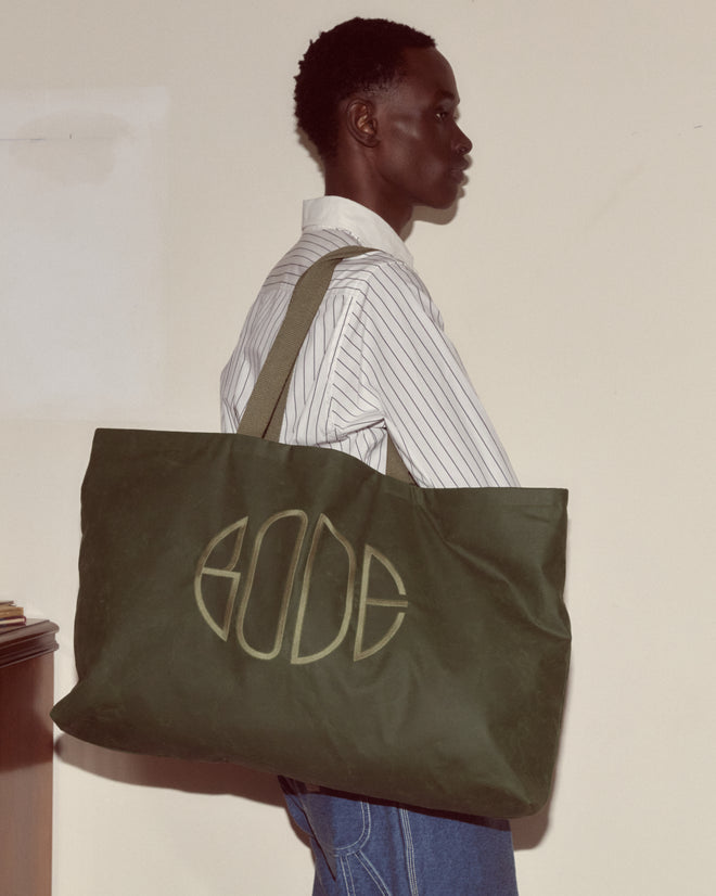 A man carrying the Waxed Cotton Zip Tote - Green, a large waxed cotton bag featuring the Bode logo embroidery, made in Italy.