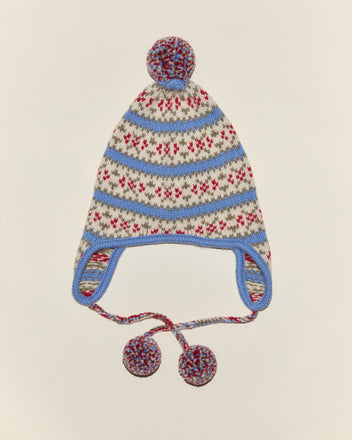 The Wedgewood Pom Hat is a cozy virgin wool knit with ear flaps, blue trim, red and blue patterns, floral accents, and pom-poms on the top and ties.