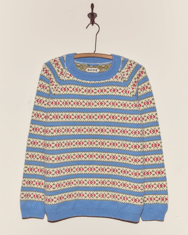 The Wedgewood Sweater, a vintage knitwear piece with blue, white, and red stripes, hangs on a wooden hanger against a plain wall.