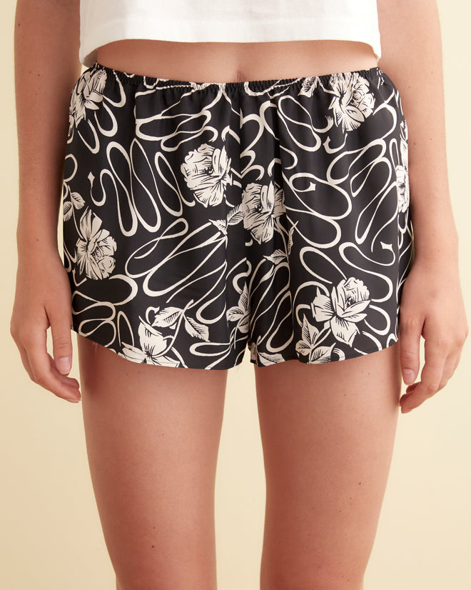 A person wearing White Rose Shorts—silky rayon shorts with a black and white floral swirl pattern—stands against a neutral background.