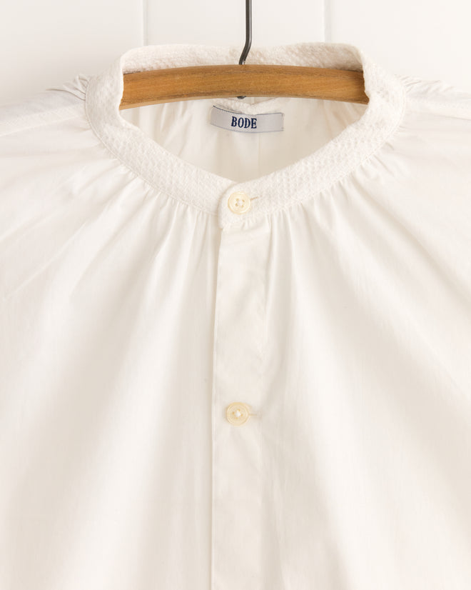 A White Smock Shirt on a hanger, featuring the "BODE" label, made from 100% cotton and inspired by historical reproductions.