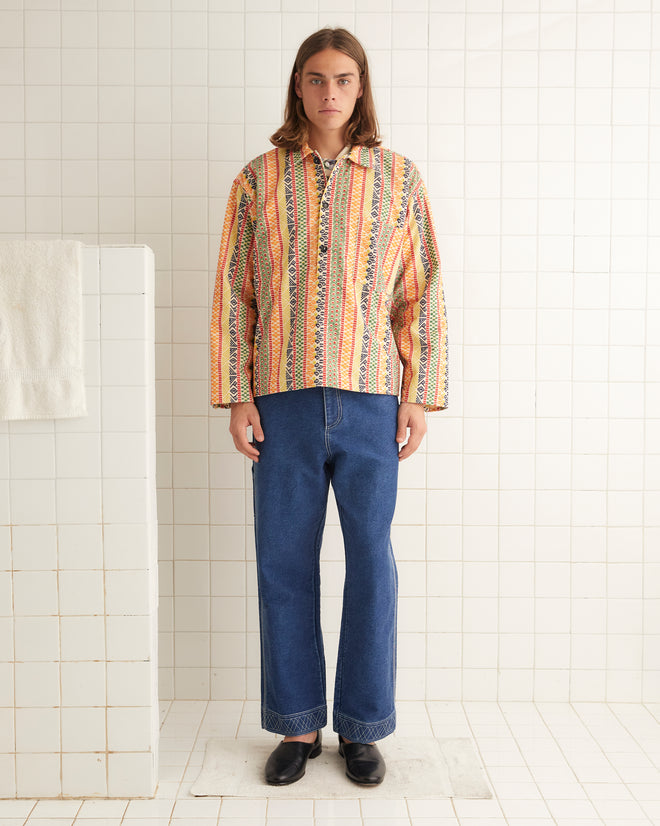 A person in a Wildflower Stripe Pullover and jeans stands in a tiled room.