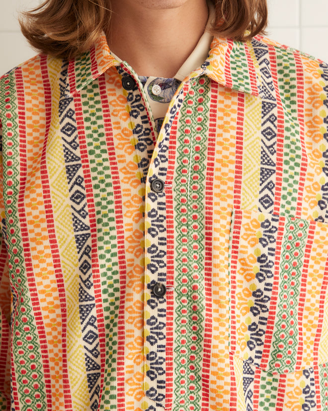 A person in a Wildflower Stripe Pullover and jeans stands in a tiled room.