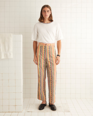 A person in a white shirt and Wildflower Stripe Trousers stands in a tiled room.