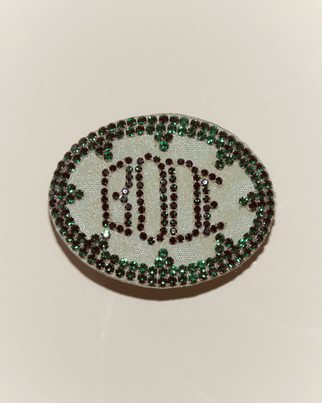 Oval brooch with “BODE” in dark stones, bordered by green and dark gemstones on a light background—perfect for pairing with the Willow Barrette - Green or complementing a Peter Pan costume.