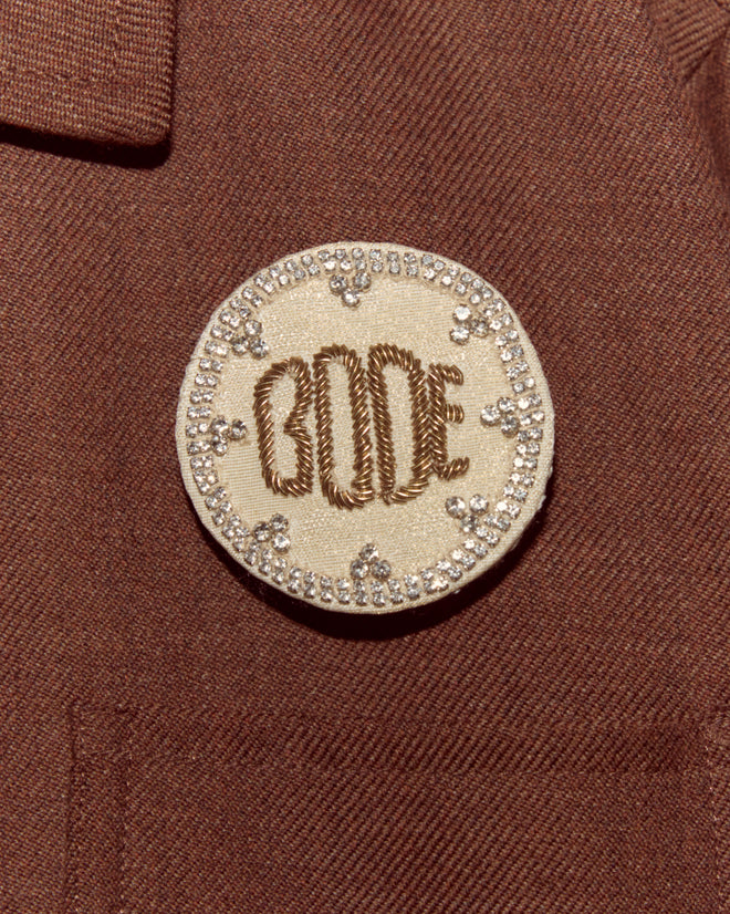 The Willow Brooch - White features a round embroidered design with rhinestones on a brown fabric background, perfect for adding a unique touch to your Bode accessories collection.