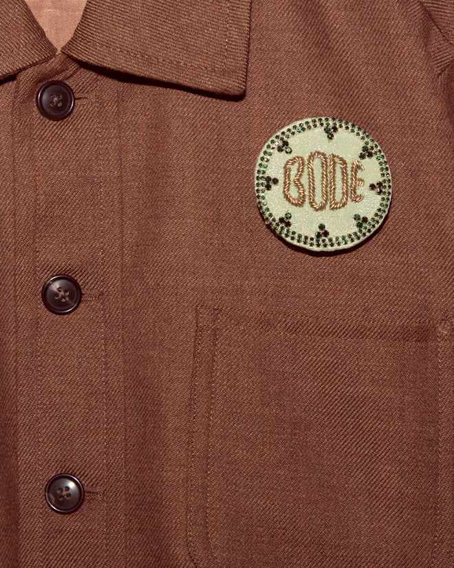 Brown button-up shirt with front pocket and a round embroidered "BODE" patch, topped with the Willow Brooch - Green for a sparkling touch of Bode accessories flair.