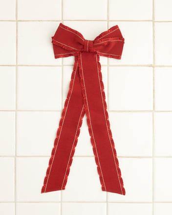 The Winner's Sash Bow, featuring a red tone and two flowing tails, is elegantly positioned on a white tiled surface.