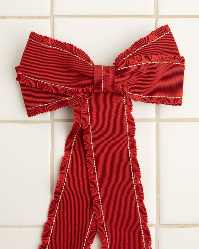 The Winner's Sash Bow, featuring a red tone and two flowing tails, is elegantly positioned on a white tiled surface.