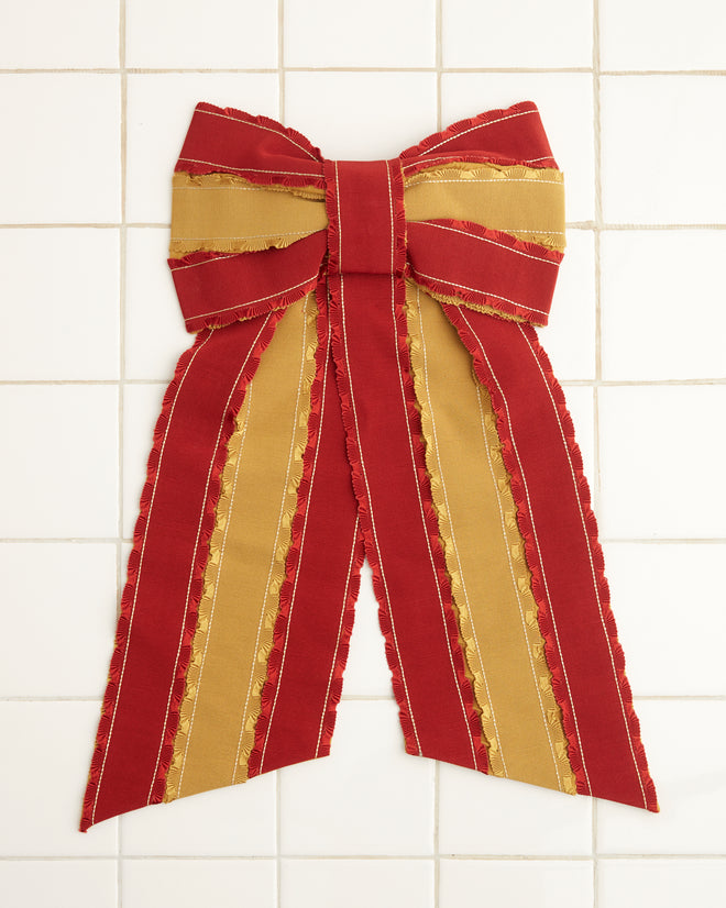 The Winner's Sash Bevel Bow, adorned with red and gold ribbons, elegantly hangs on a tiled wall, adding a touch of historical reproduction charm.