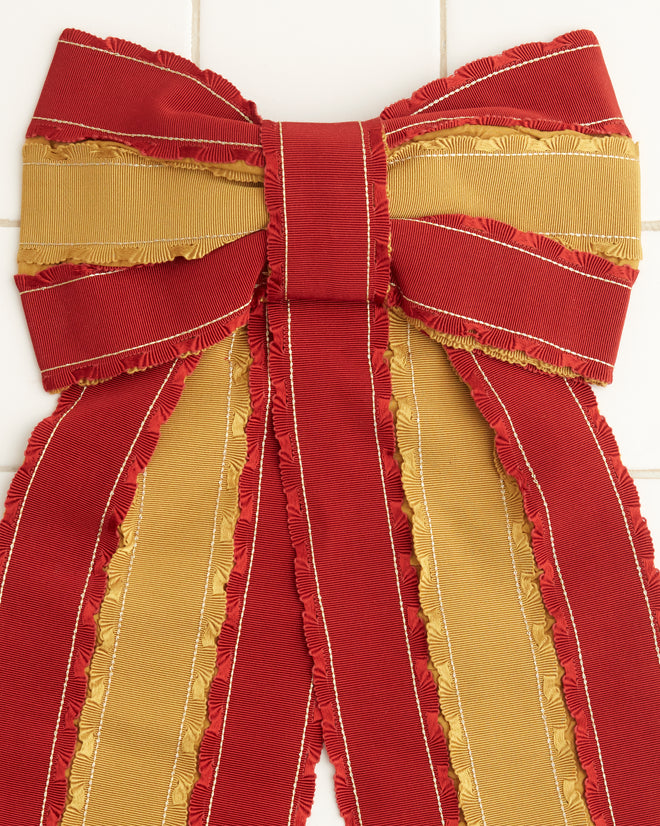 The Winner's Sash Bevel Bow, adorned with red and gold ribbons, elegantly hangs on a tiled wall, adding a touch of historical reproduction charm.