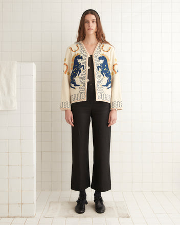 A person wearing the Winter Stallion Jacket and black pants stands against a tiled wall in a minimalistic setting.