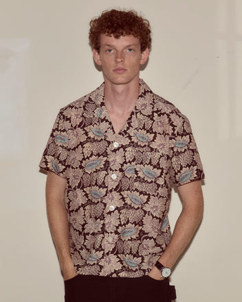 A man with curly hair wears the Wisteria Short Sleeve Shirt, standing against a plain beige background.