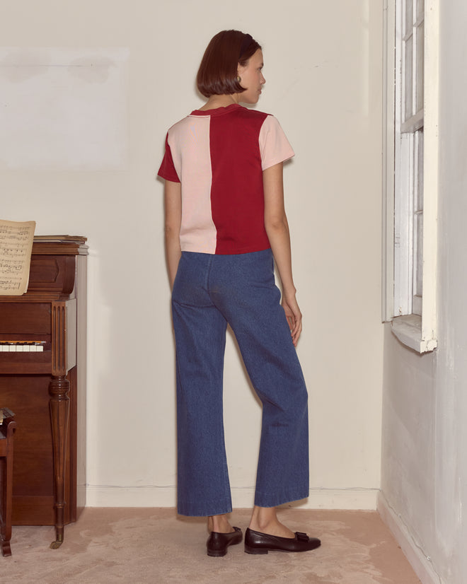 A woman with short brown hair stands indoors, back to the camera, wearing the Wonderland Tee with a hearts motif, paired with jeans and loafers.
