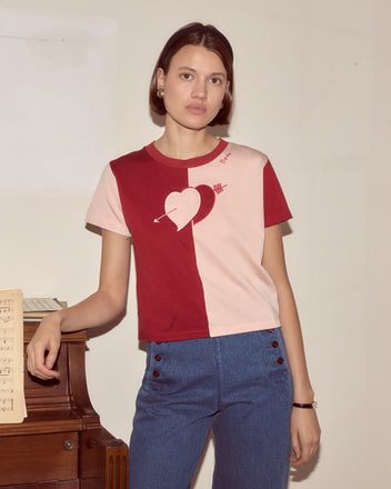 Woman in a Wonderland Tee with blue pants stands by a piano and sheet music, channeling an Alice Through the Looking Glass vibe as she looks at the camera.