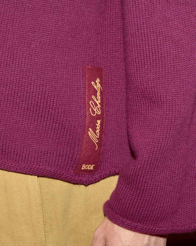 Close-up of the Wool Dock Pullover, a chunky purple virgin wool sweater with a brown label reading "Maison Chardog" and "BODE," paired with tan pants.