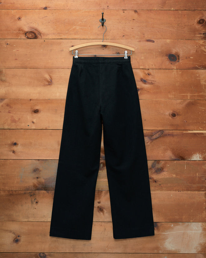 Denim Sailor Trousers - Black displayed on a wooden hanger, set against a wooden plank wall.
