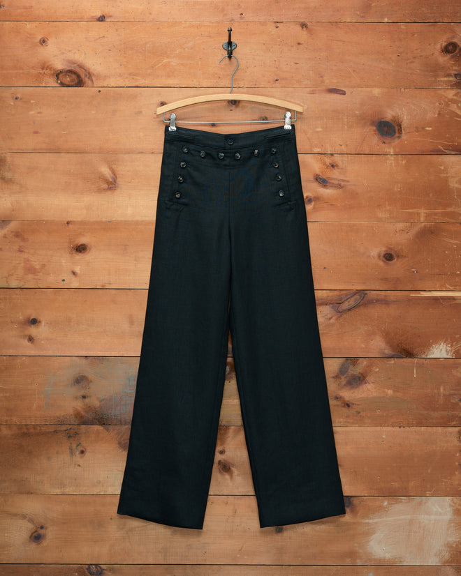 Linen Sailor Trousers - Black, featuring a wide-leg silhouette and decorative buttons inspired by 1940s style, displayed on a wooden hanger against a wood wall.