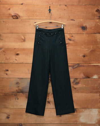 Linen Sailor Trousers - Black, featuring a wide-leg silhouette and decorative buttons inspired by 1940s style, displayed on a wooden hanger against a wood wall.