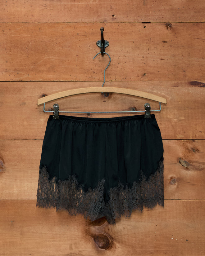 Black Lace Inlay Tap Shorts in 1930s style with wide lace trim, hanging on a wooden hanger.