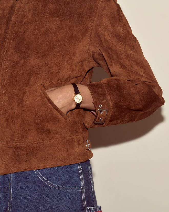 Person wearing the Suede Howard Jacket - Dark Brown, blue jeans, and a gold wristwatch with a brown strap on their left wrist.