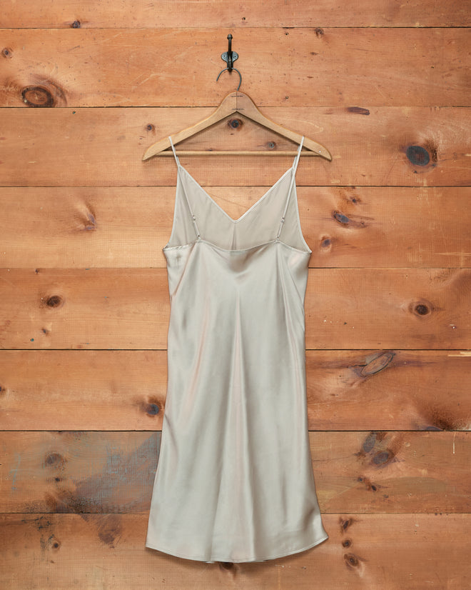 An ivory Lizzie Short Slip, crafted from 100% silk, hangs on a wooden hanger against a rustic wooden wall.