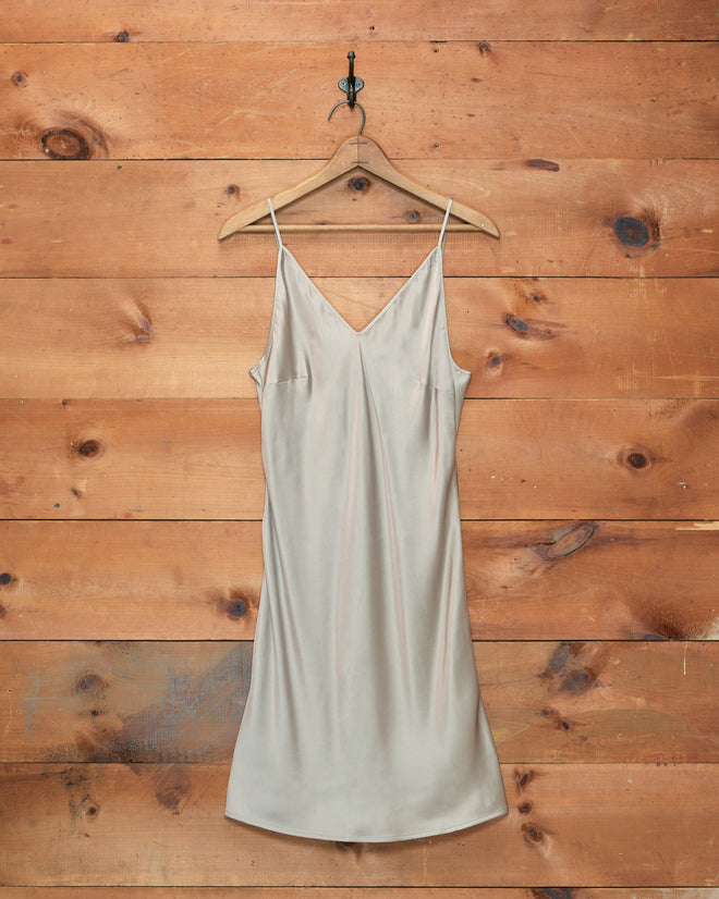 Lizzie Short Slip in Ivory, crafted from 100% silk and made in Portugal, displayed on a hanger against a rustic wooden wall background.