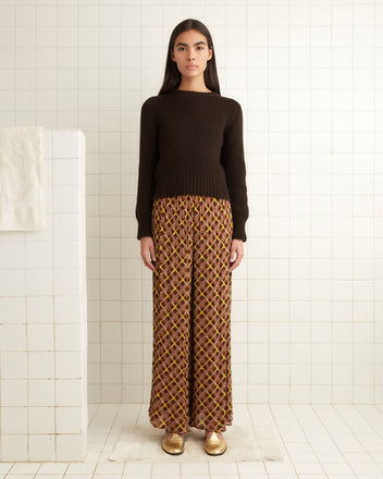 A person in a brown sweater and Cattail Plaid Pants is standing in a tiled room.