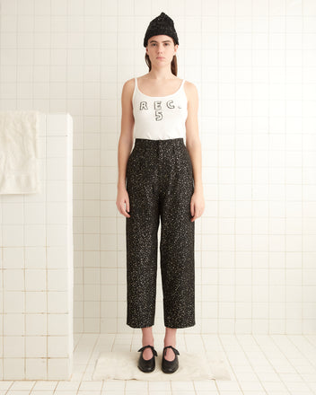 A person is standing in a tiled room wearing a white tank top, the Glitter Murray Trousers, a beanie, and shoes. The trousers are adorned with eye-catching glitter dots that add a touch of sparkle to the look.