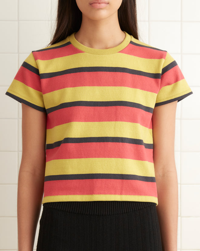 A person wearing a Rec Stripe Tee and black shorts is standing in a tiled room with a towel hanging on the wall.