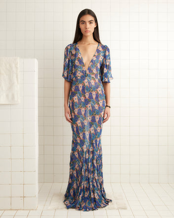 A woman in a 1930s-inspired Daisy Fair Gown stands in a tiled room with a neutral expression, highlighting its subtle overlapping floral pattern.