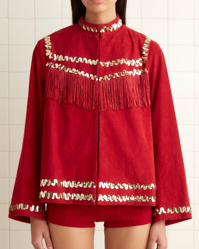 A person in a striking Bandstand Fringe Jacket paired with gold shoes stands in a tiled room, where a towel hangs neatly on the rack.