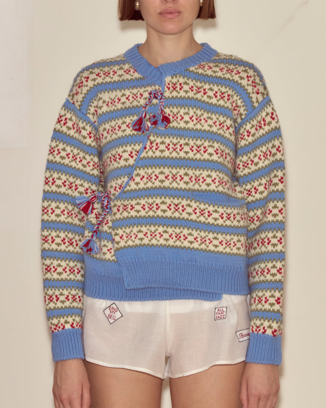 Person wearing the Wedgewood Cardigan, a patterned knit virgin wool design with tassels, paired with white shorts and standing against a plain background.