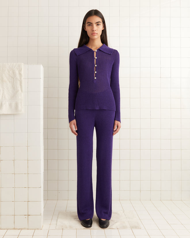 A person stands in a bathroom wearing Quincy Joggers - Purple, paired with a matching long-sleeve top with buttons, in front of a tiled white wall.