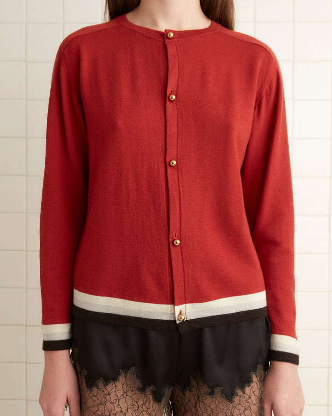 A person in a cozy Fairground Cardigan - Red and black lace shorts stands in a tiled room, wearing black socks and shoes.