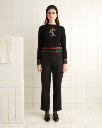 A woman wearing a Ski Run Crewneck with colorful trim stands in the tiled room.