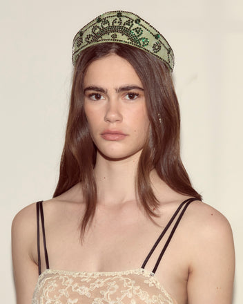 Woman with long brown hair wears the Willow Crown - Green, a jeweled headband adorned with rhinestones, paired with a lace dress featuring thin black straps.