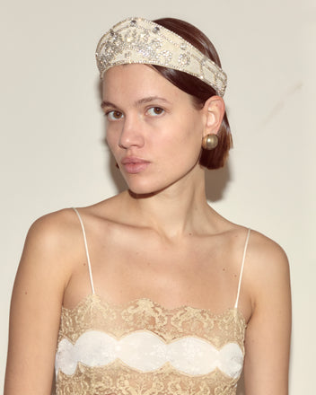 Woman wearing the Willow Crown - White rhinestone headpiece and gold earrings, dressed in lace, gazes at the camera against a plain background.