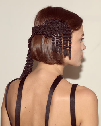 A woman with short brown hair, seen from behind, wears a black strap dress and decorates her hair with the Jet Braid Barrette.