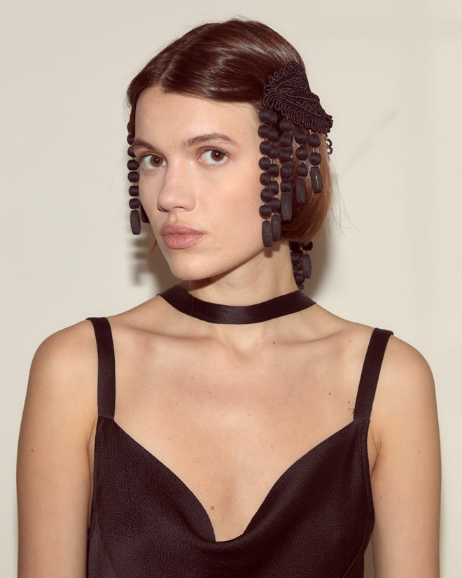 Woman in a black dress wears the Jet Braid Barrette as a decorative black hair accessory, looking at the camera.
