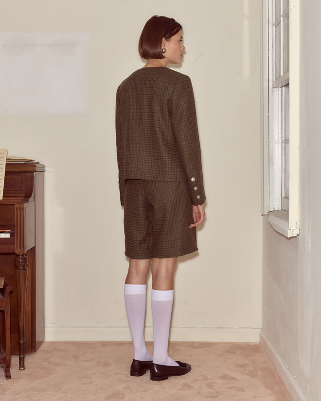 A person in a brown checkered suit and white knee-high socks stands near a window, wearing the Morris Houndstooth Shorts with D-ring waist adjusters.
