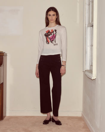 Indoors, a person looks at the camera wearing the Cheval Long Sleeve Tee with an illustrated horse design and abstract colorblocking, paired with black pants and black shoes.