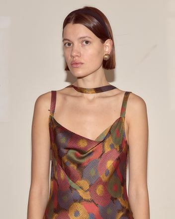 Woman wearing the Fruit Pit Dress, a colorful silk seersucker style, paired with a matching choker and gold earrings, against a plain background.