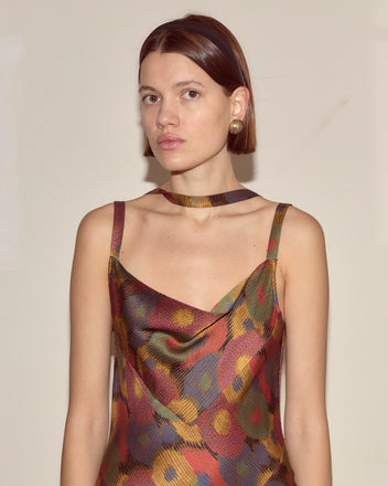 Woman wearing the Fruit Pit Dress—a colorful 100% silk seersucker piece—paired with a choker, standing against a plain light background and looking at the camera.
