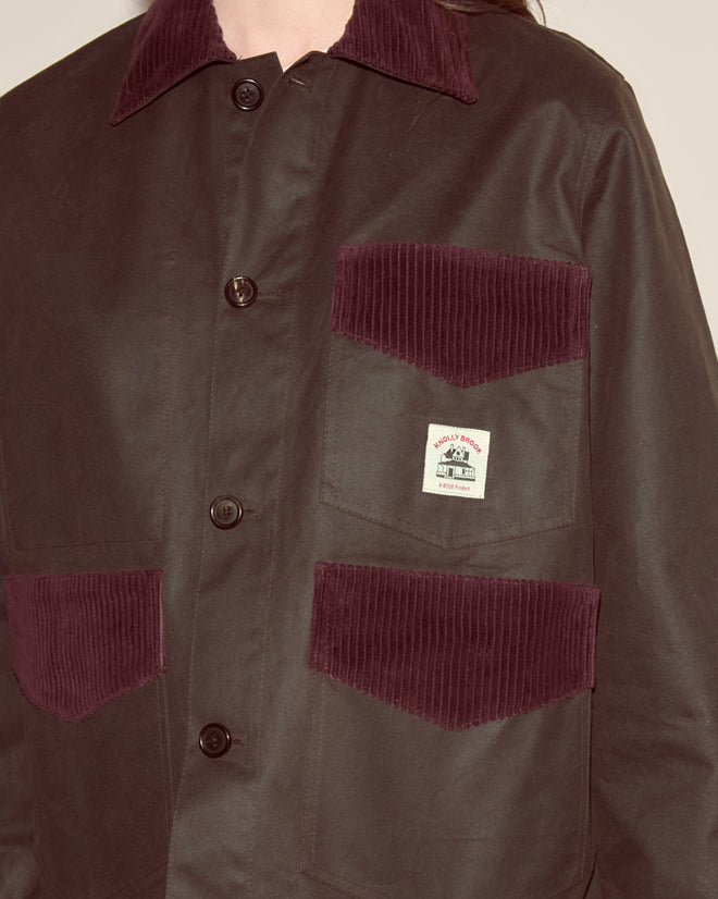 The Waxed Craft Jacket - Brown features dark maroon corduroy trim on the pockets and collar, a button-up front, and a label on the chest pocket.