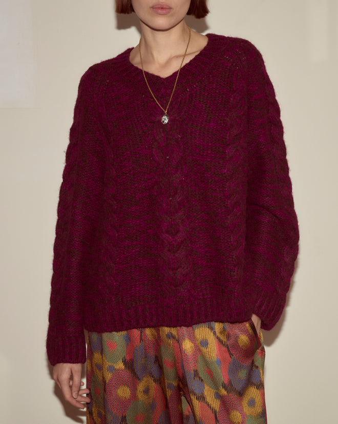 Person wearing the Eiderdown Sweater - Maroon, featuring a textured maroon baby alpaca design, paired with colorful patterned pants and a pendant necklace.